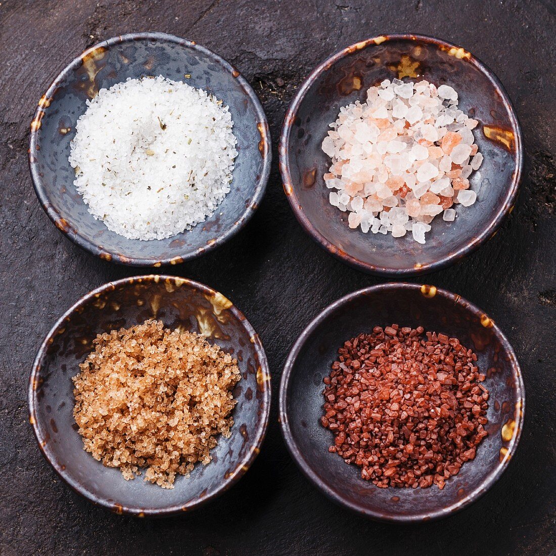 Different types of food coarse Salt in ceramic bowls on dark background
