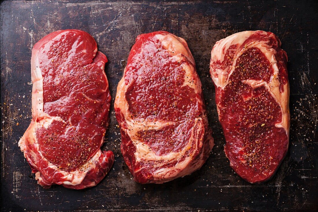 Three cuts of Raw fresh meat Steaks and seasonings on dark background