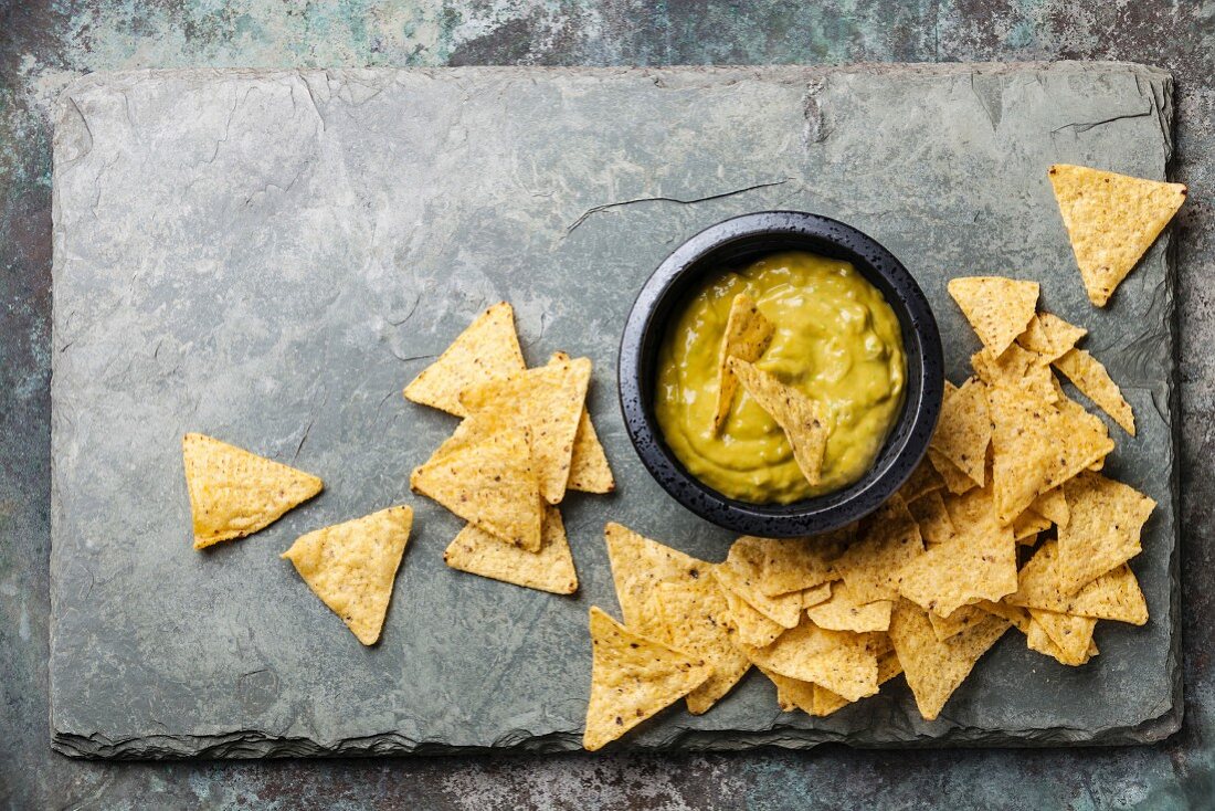 Fresh guacamole dip with nachos chips on stone slate background