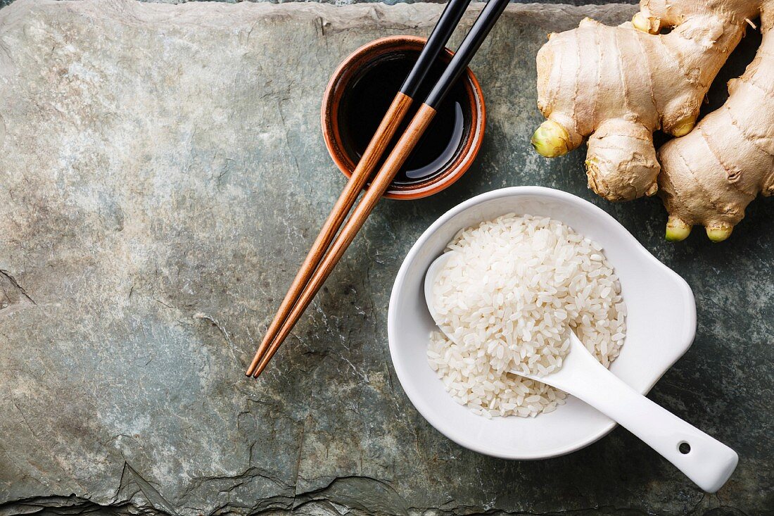 Reis, Ingwer, Sojasauce und Sushi-Stäbchen auf grauem Schieferuntergrund