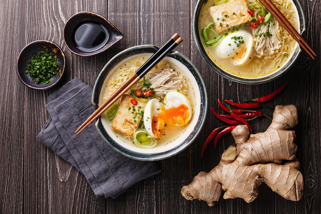 Asian Miso ramen noodles with egg, tofu and enoki in bowls on gray wooden background