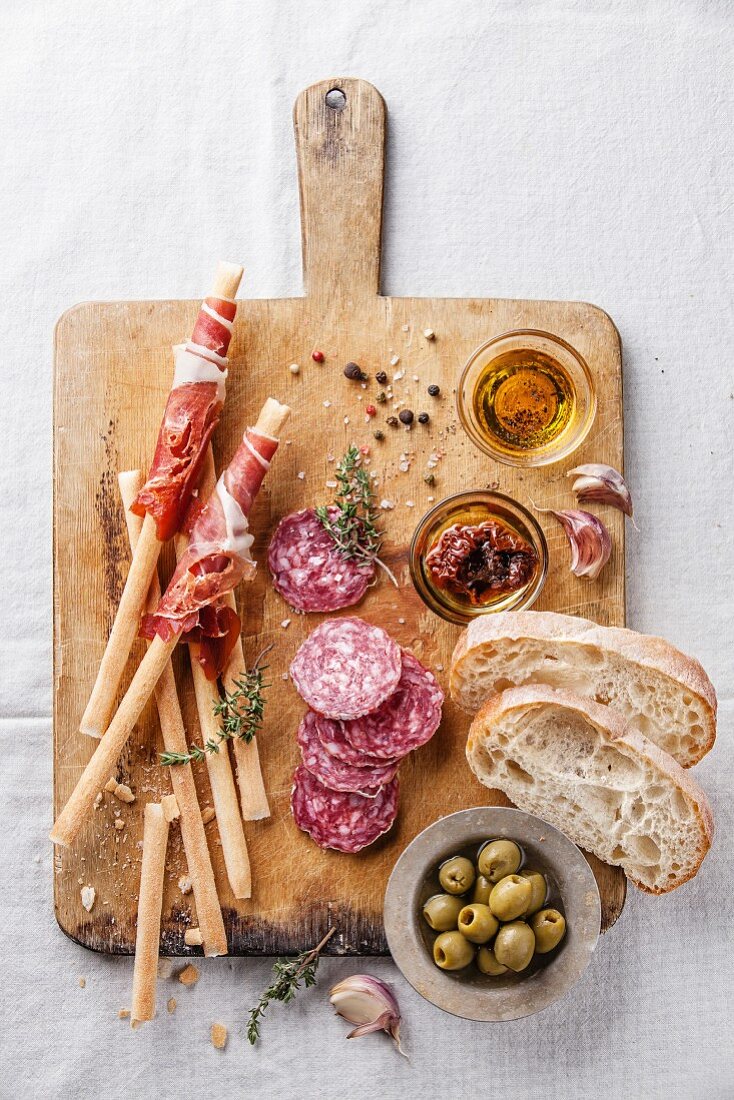 Antipasti: Grissini mit Schinken, Salami, Oliven und Brot auf Holzbrett