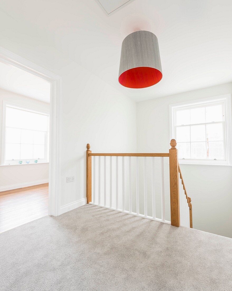 An empty staircase with grey carpet and a wooden railing, with an orange lampshade above