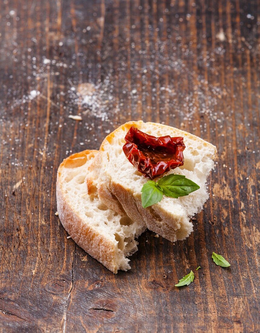 Eine halbierte Scheibe Ciabatta mit getrockneter Tomate und Basilikum