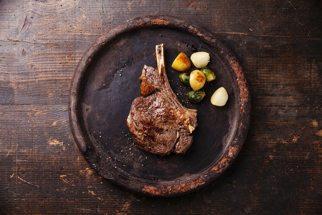 Ribeye Steak on bone with vegetables on stone plate on wooden background