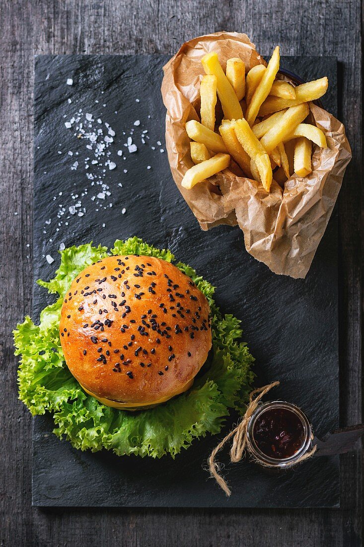 Fresh homemade hamburger with black sesame seeds and french fries potatoes in backing paper