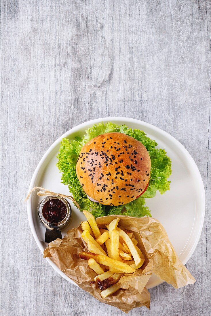 Fresh homemade burger with black sesame seeds in white plate with fried potatoes