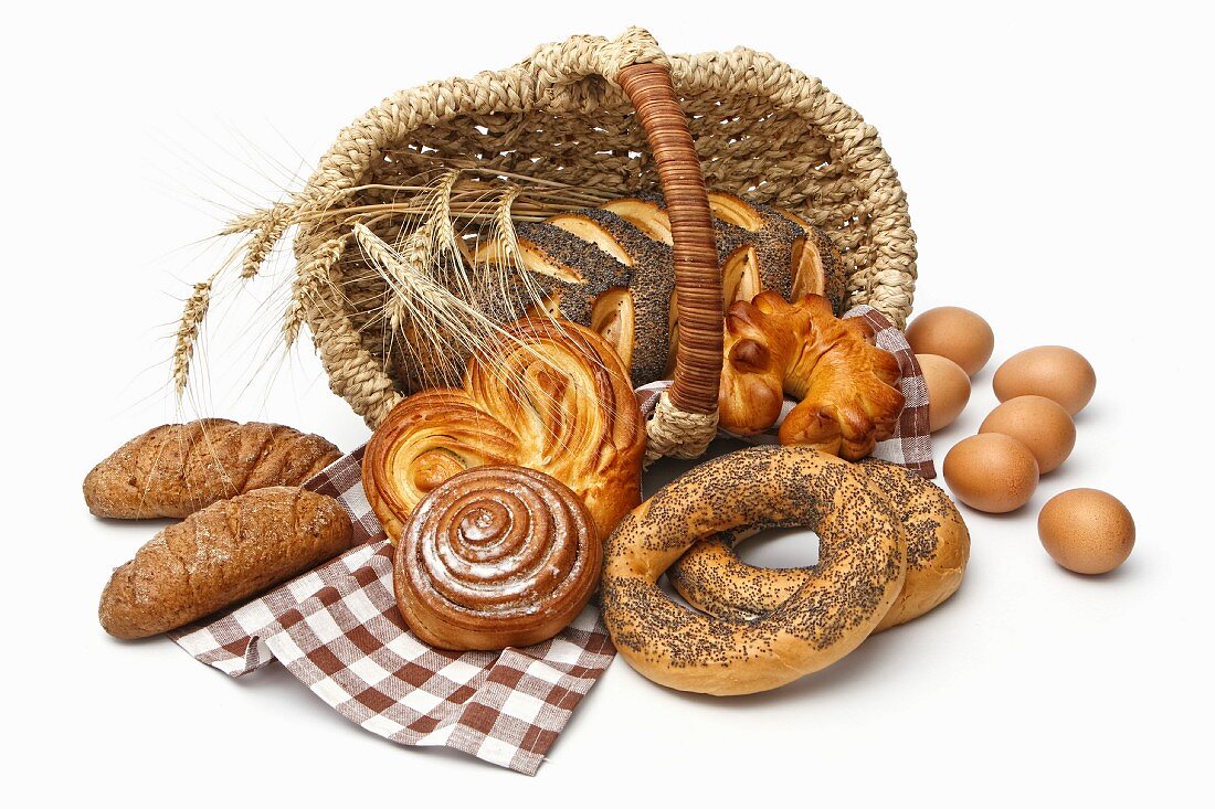 Assortment of baked bread with wheat in basket isolated on white background