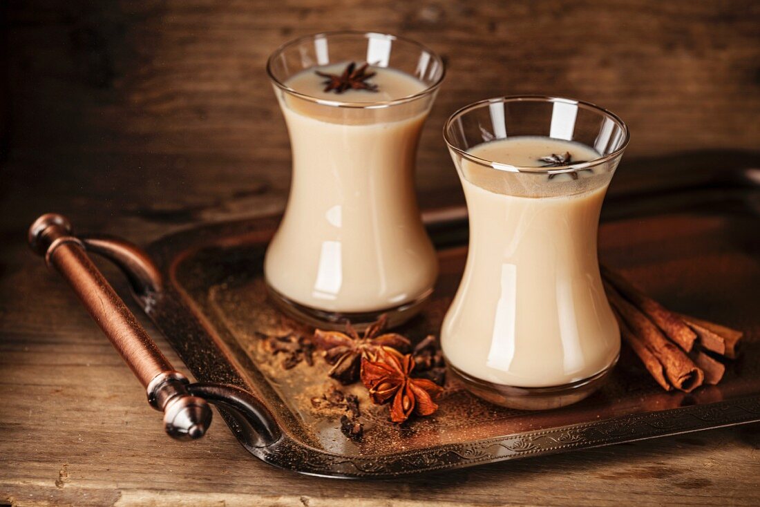 Hot tea with milk and spices on dark background