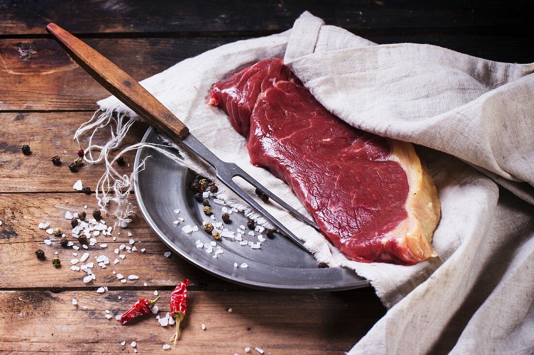 Rohes Steak auf Metallteller an altem Holztisch