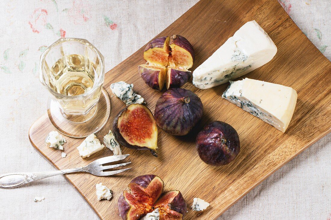 Figs with blue cheese, white wine and crackers on wooden cutting board