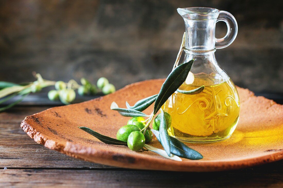 Bottle of olive oil with olive branch in handmade clay plate over wooden table