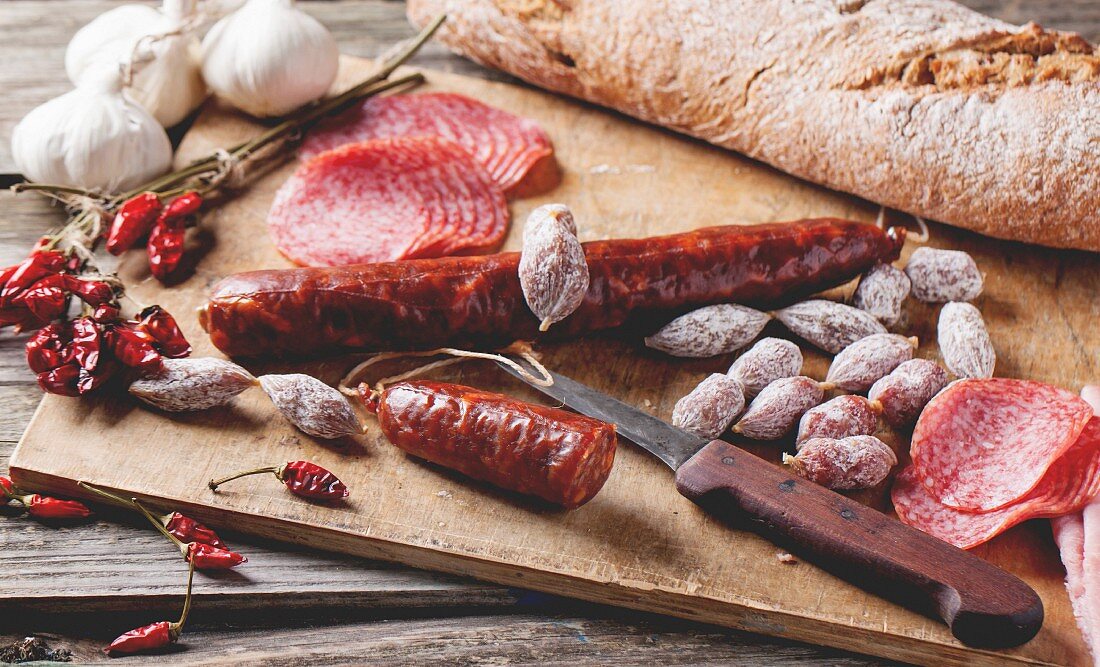 Set of salami sausages served with fresh bread, garlic and red hot chili peppers on wooden cutting board