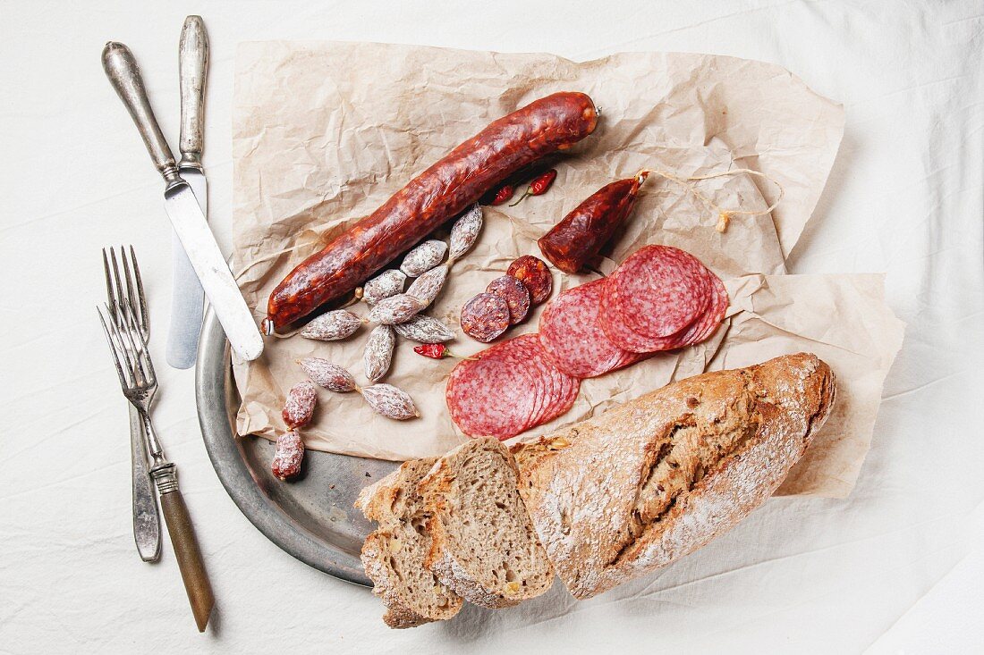 Vintage tray with set of salami sausages with fresh bread and red hot chili peppers