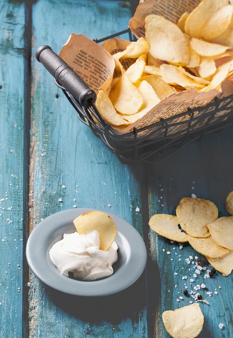 Kartoffelchips in Drahtkorb und Dip auf blauem Holztisch