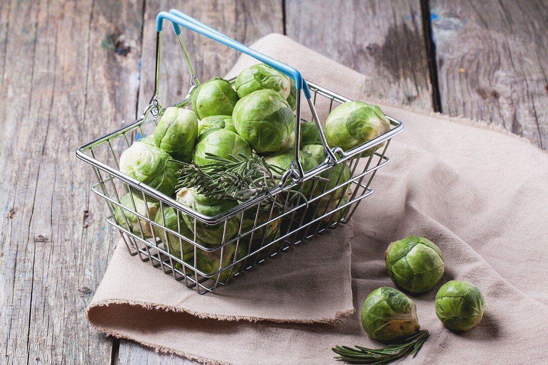 Food basket of brussels sprouts and rosemary on old wooden table