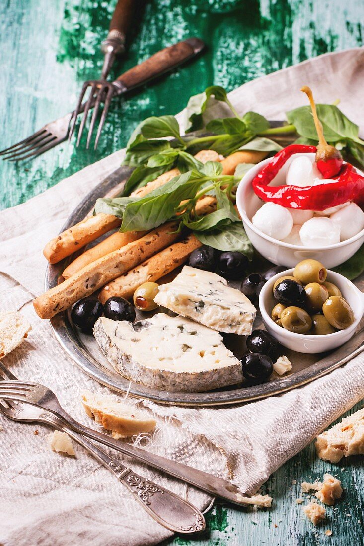 Gemischte Antipasti Blauschimmelkäse, Oliven und Mozarella serviert auf silbernen Tablett an grünem Holztisch