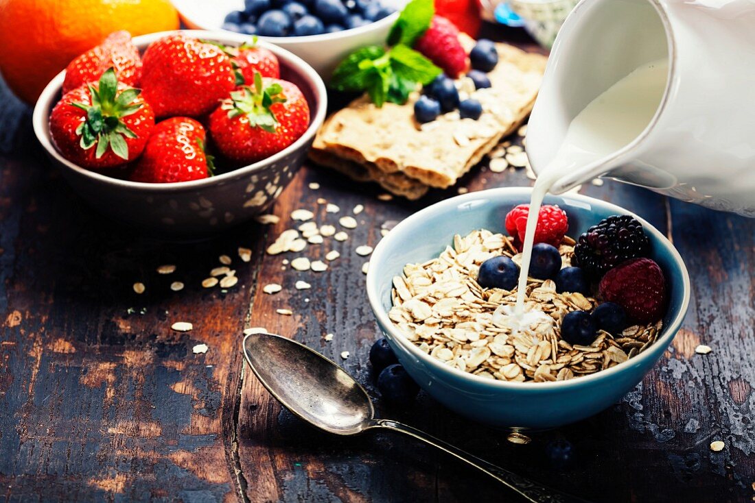 Diet breakfast: Bowls of oat flake, berries and fresh milk on wooden background