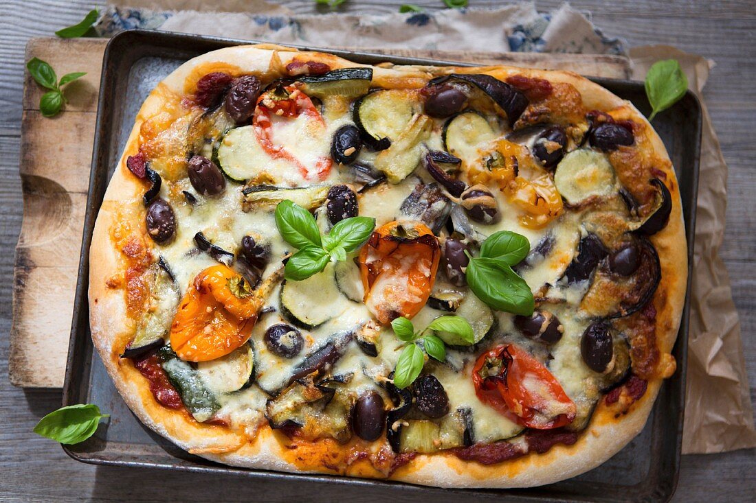 Selbstgemachte Pizza mit gebratenem Gemüse, Oliven und Basilikum