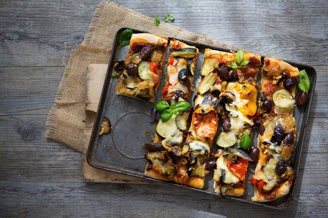 Selbstgemachte Pizza mit gebratenem Gemüse, Oliven und Basilikum auf Backblech