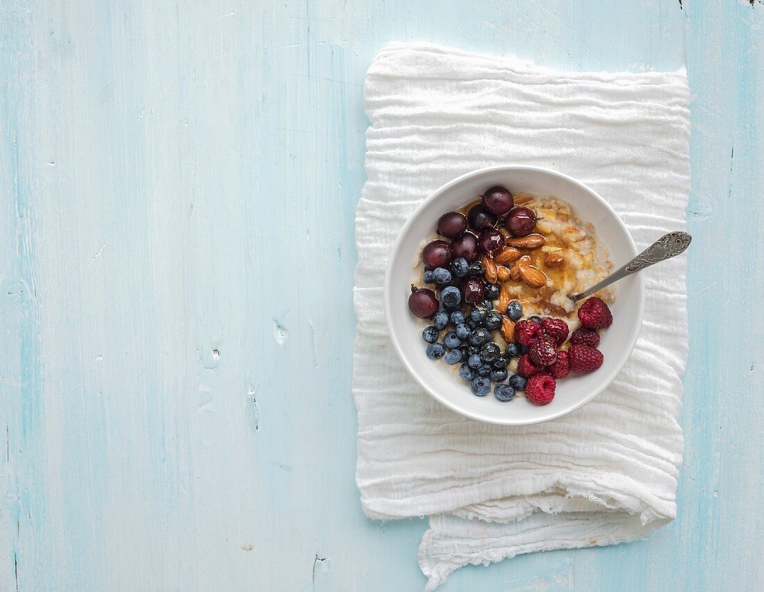 Healthy breakfast set. Bowl of oat porridge with fresh berries, almond and honey over white napkin