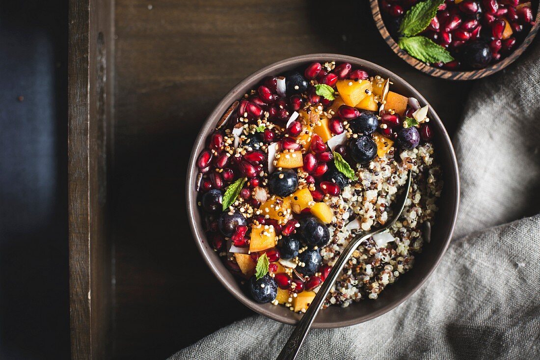 A bowl of coconut quinoa porridge, pomegranate seeds and sliced apricots