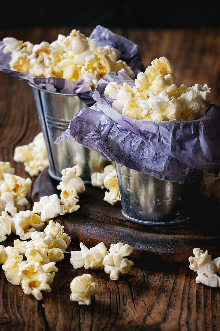 Prepared salted popcorn served in small buckets with paper inside on wood chopping board