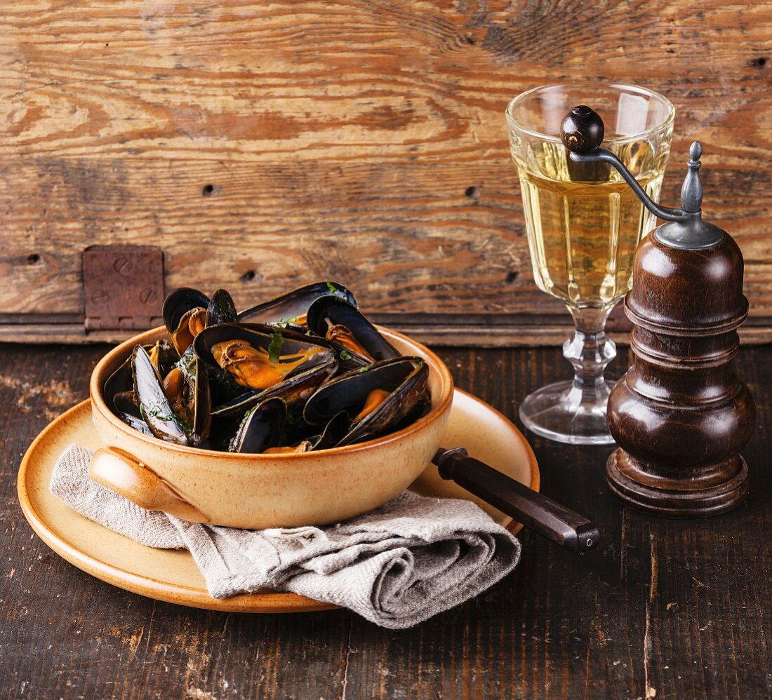 Mussels clams in bowl and white wine on wooden background