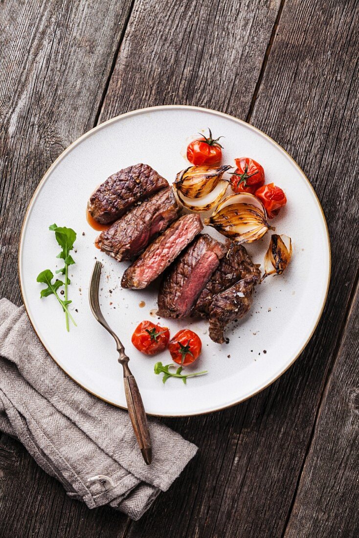 Sliced medium rare grilled Beef steak Ribeye with grilled onions and cherry tomatoes on plate