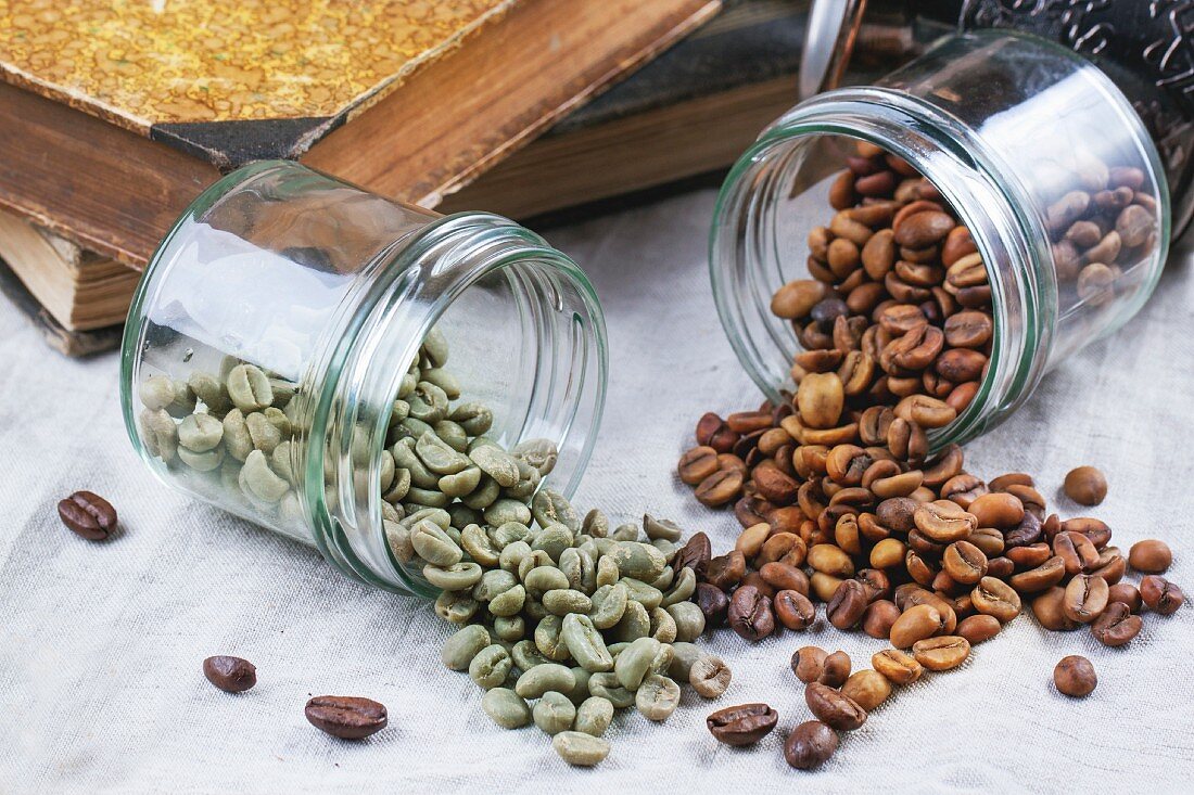 Grüne und braune entkoffeinierte Rohkaffee-Bohnen in umgefallenen Gläsern