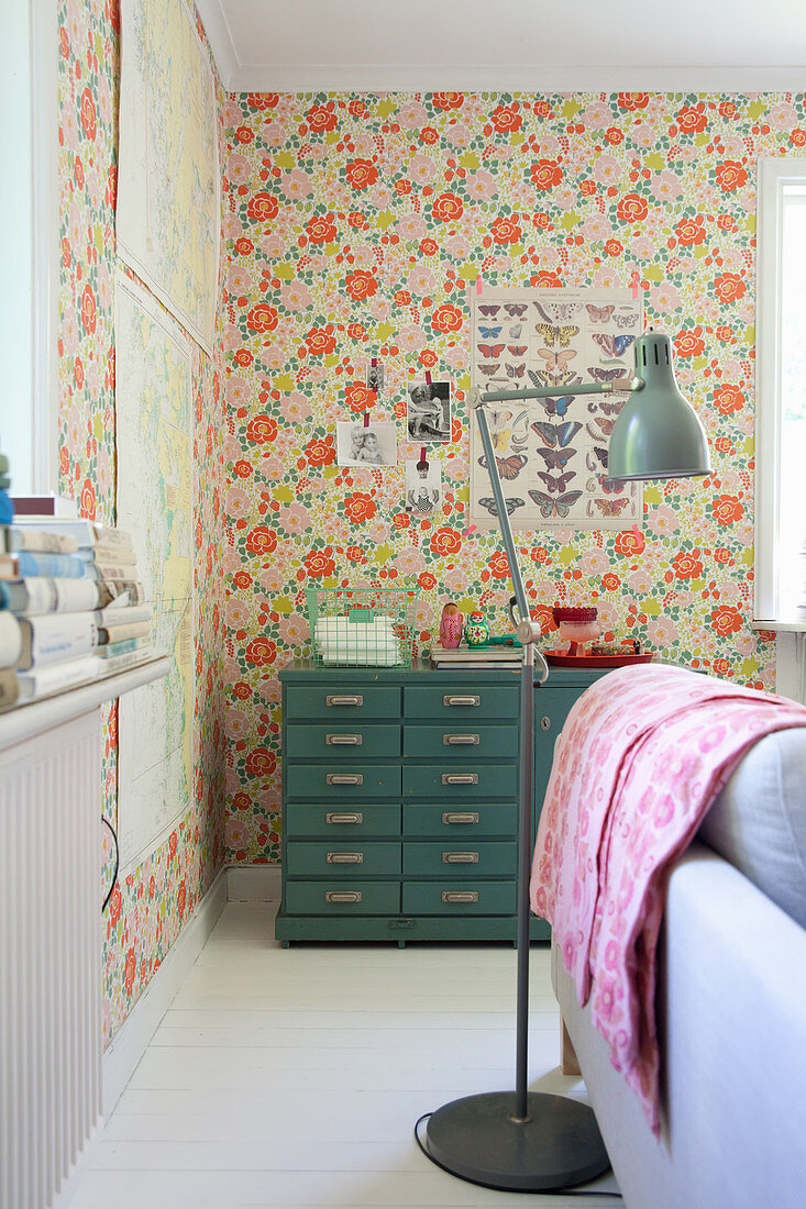 Industrial-style lamp and chest of drawers against floral wallpaper