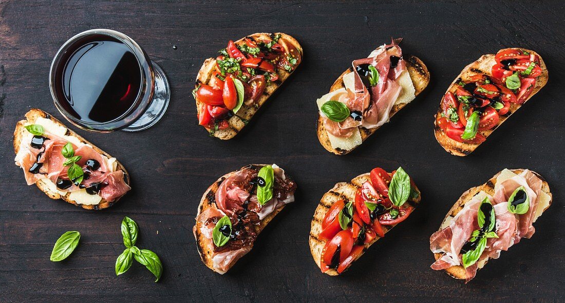 Brushetta snacks for wine. Variety of small sandwiches and glass of red wine on dark rustic wooden backdrop