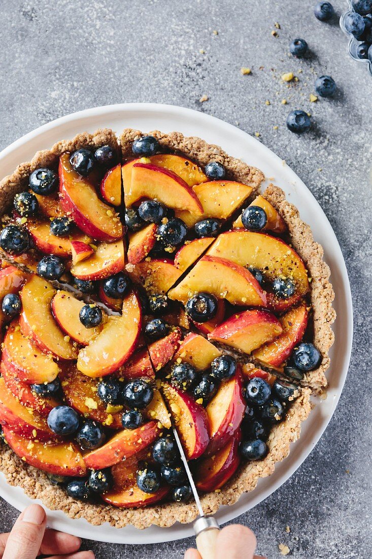 A woman is slicing a peach and blueberry tart with a knife