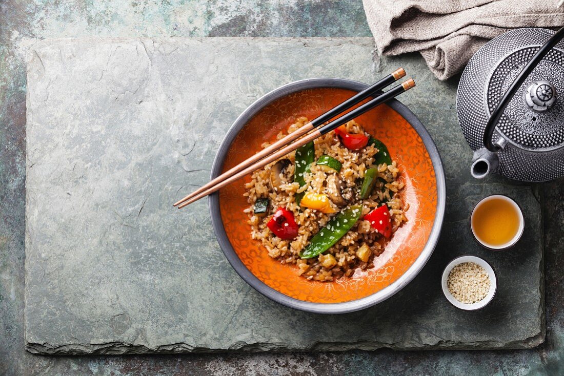 Fried Rice with vegetables in red bowl and green tea on stone slate background
