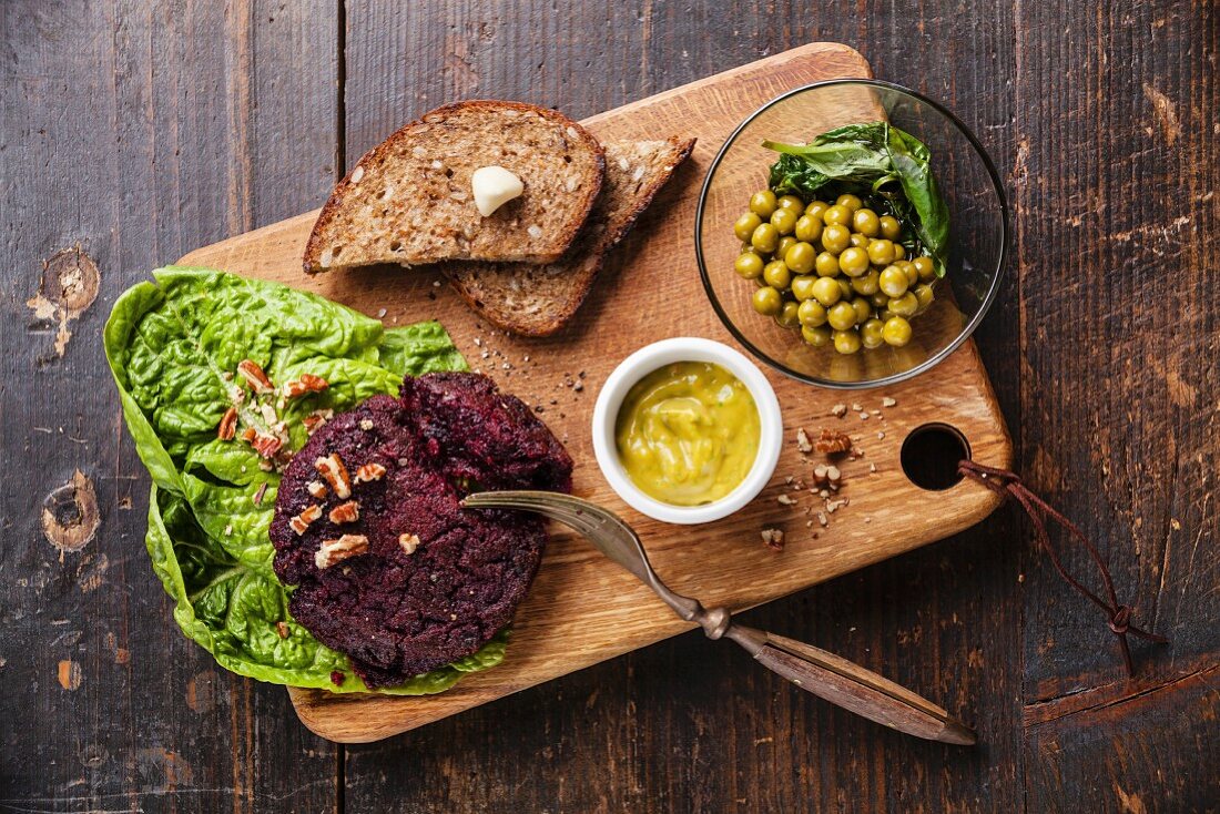 Veganes Schnitzel aus Roter Bete serviert mit grünem Erbsen-Salat auf Holzbrett