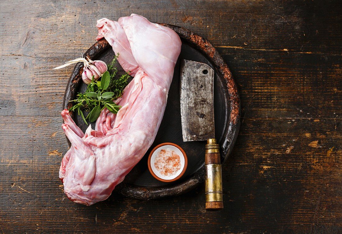 Raw whole rabbit and meat cleaver on dark wooden background