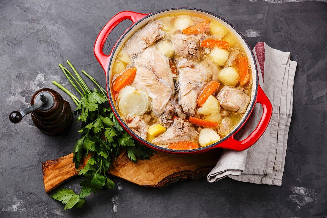 Stewed rabbit with potatoes and carrot in cast iron pot on concrete background