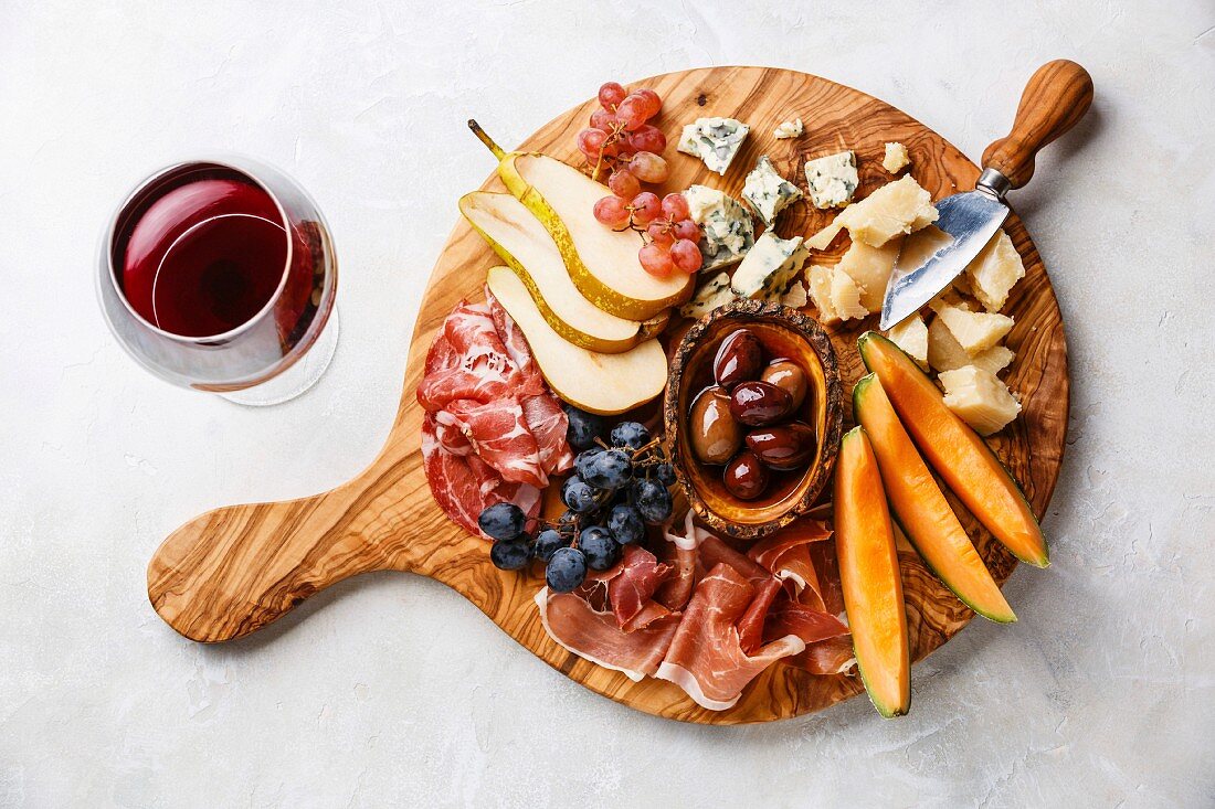 Antipasti-Platte mit Schinken, Käse, Obst und Oliven dazu ein Glas Rotwein