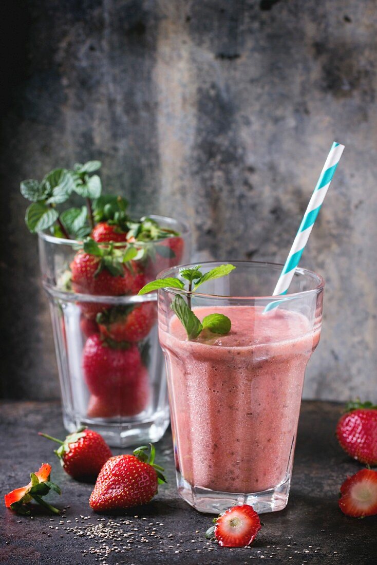 Ein Glas Erdbeer-Smoothie mit Chiasamen, serviert mit Trinkhalm, frischer Minze und Erdbeeren