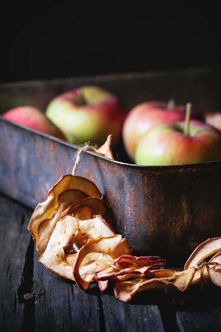 Getrocknete Apfelringe auf Schnur an alter Backform, Hintergrund Äpfel