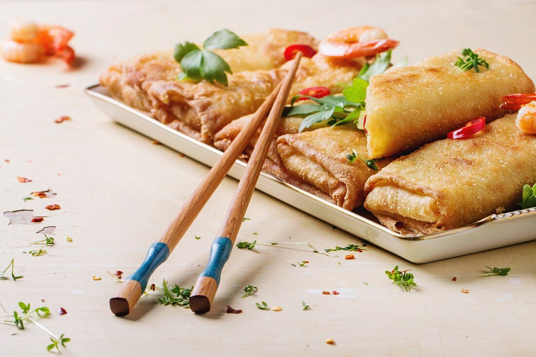 Fried spring rolls with vegetables and shrimps, served with spicy sauce and chopsticks over white wooden background
