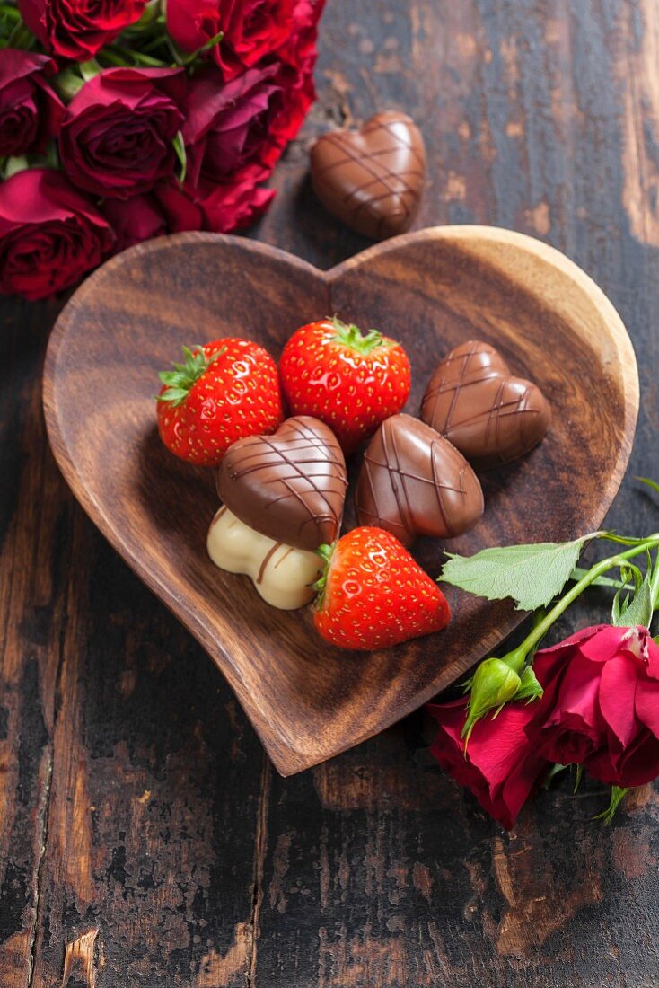 Heart shape plate with strawberries and chocolate on wooden table