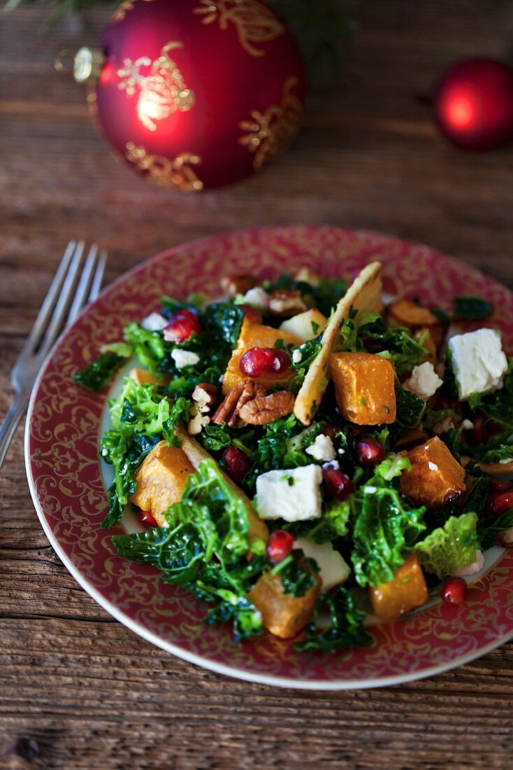 Festive kale, roasted sweet potatoes and parsnips salad with Feta cheese, pecans and pomegranate in a bowl