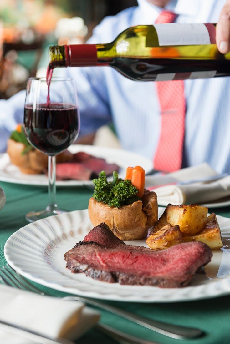 Roastbeef mit Yorkshire Pudding, Gemüse und Wein auf Restauranttisch