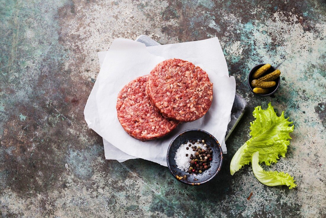 Raw Ground beef meat Burger steak cutlets and seasonings on metal background