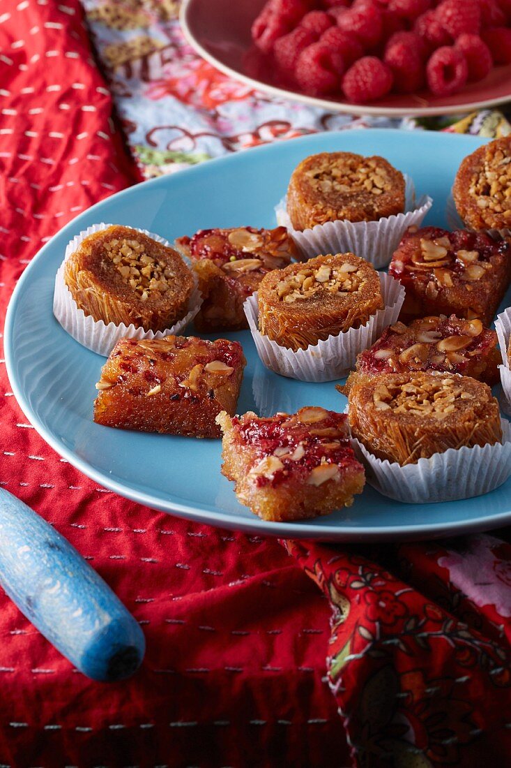 Raspberry namoura and brazil nut bourma baklava on ethnic floral tablecloth with fresh raspberries