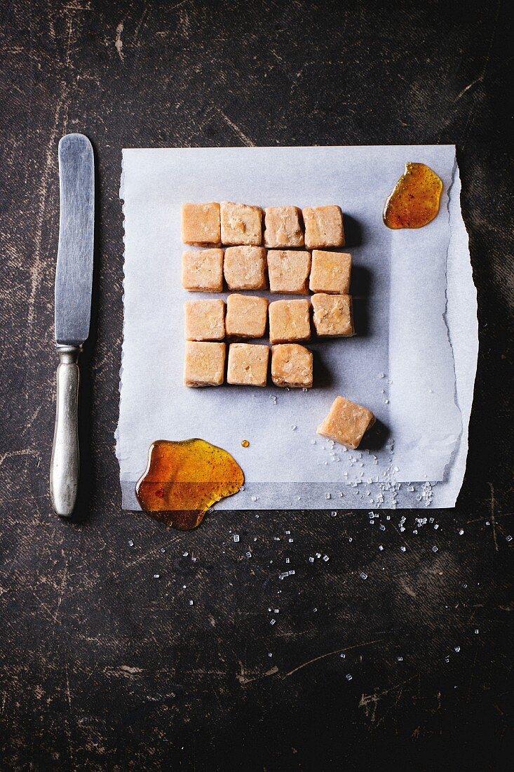 Fudge candy and caramel on baking paper, served with vintage knife over dark background