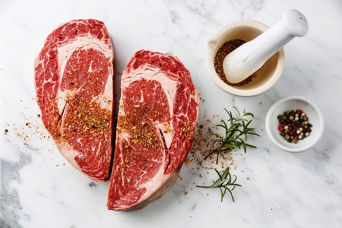 Zwei rohe Ribeye Steaks in Herzform mit Kräutern und Gewürzen