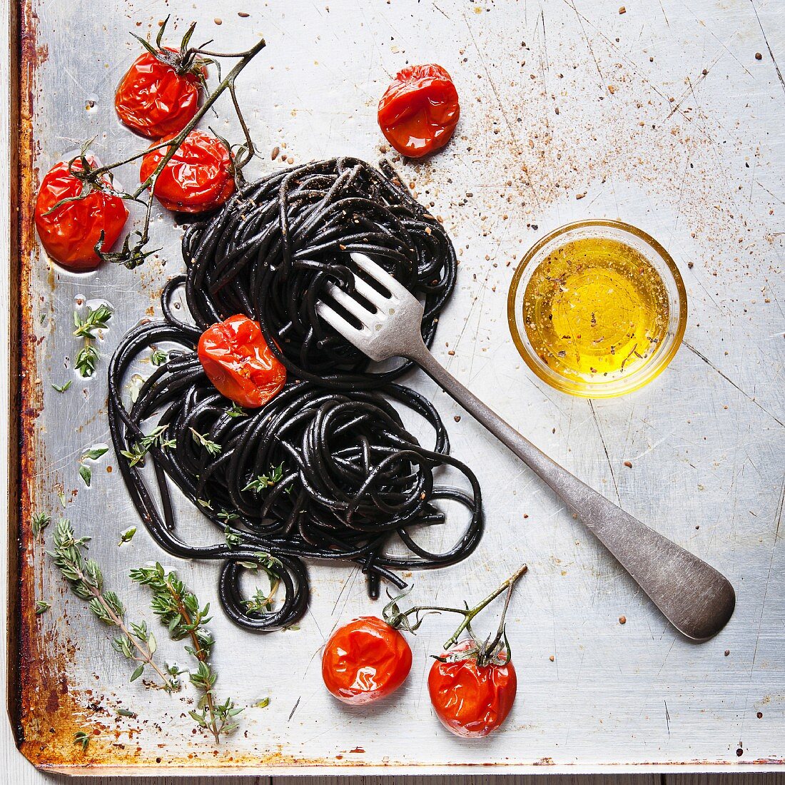 Schwarze Spaghetti mit Ofentomaten auf Ofenblech (Aufsicht)