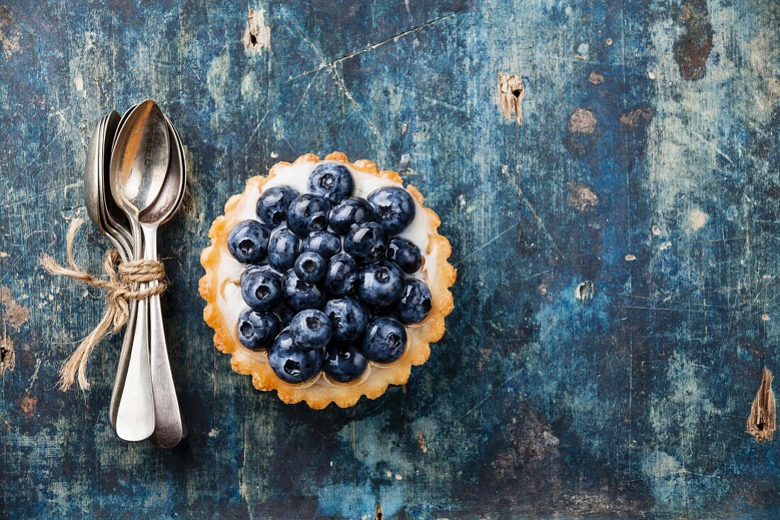 Blueberry tart and Bunch of teaspoons on blue wooden background